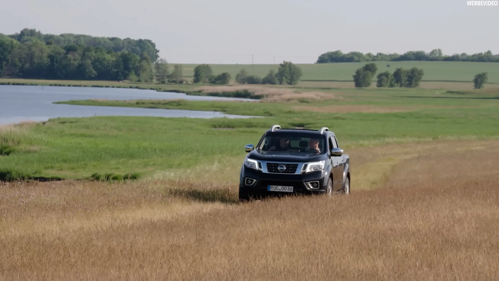Pick-up auf einem Feldweg zwischen Wiese und See