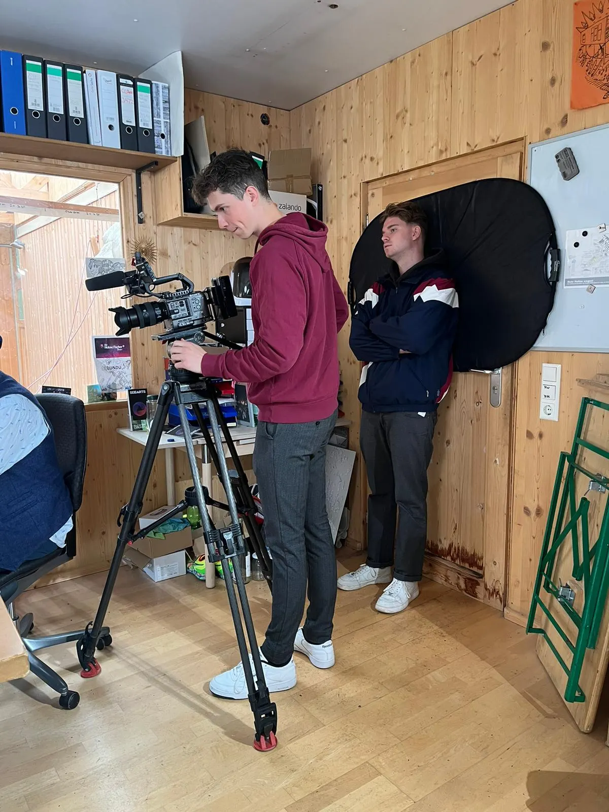 Kameramann filmt zwei Personen vor einer Holzwand, daneben eine Softbox