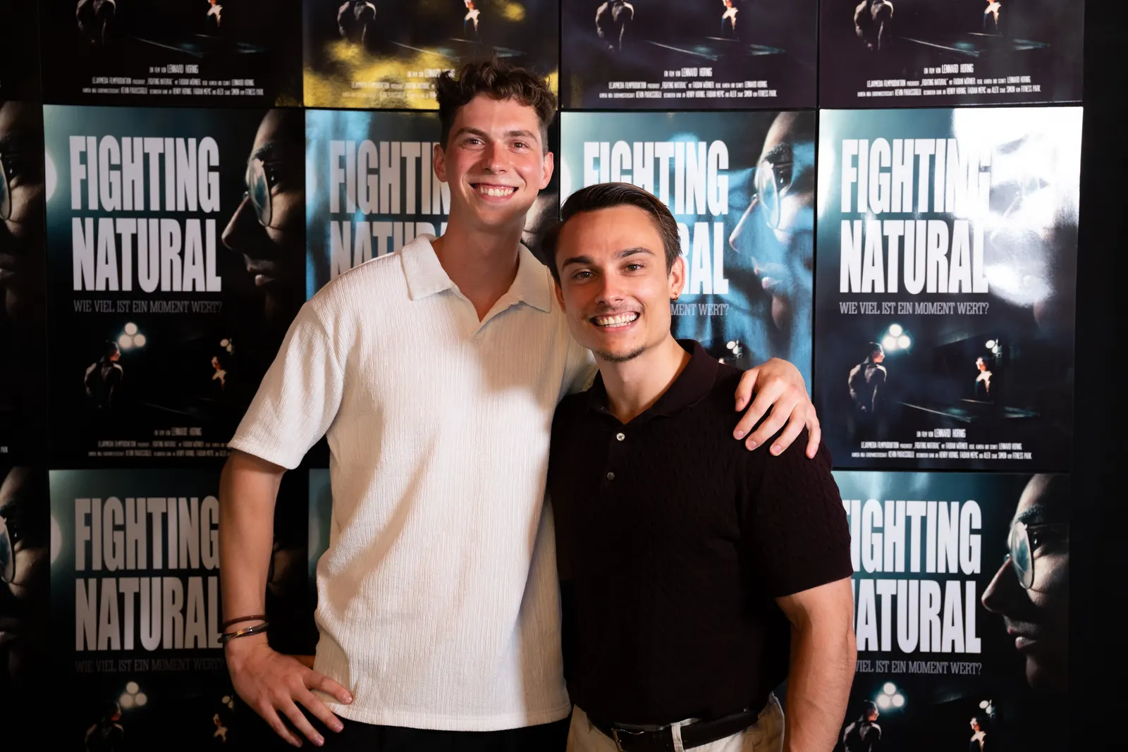 Zwei Männer vor einer Plakatwand mit Fighting-Natural-Postern